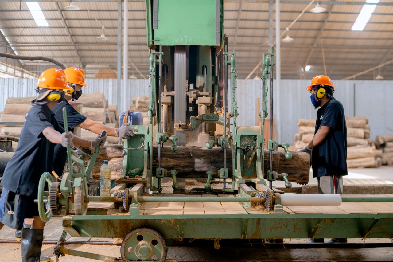 cta-image Industrial lumber processing with workers operating machinery in a factory setting.