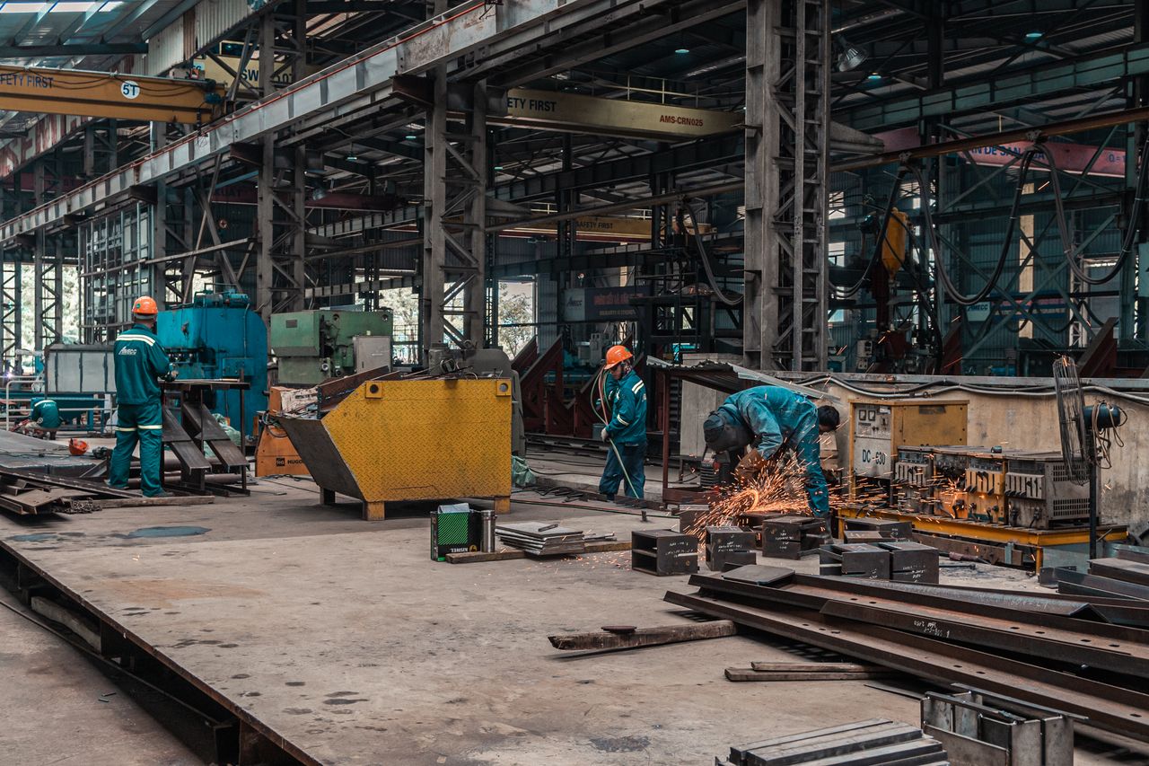 our-services-01 Workers in a metal workshop engaged in active construction and welding tasks.